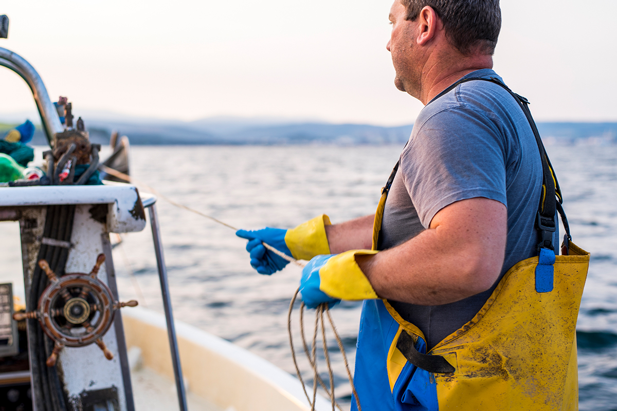 A fisherman stands on a boat in the ocean, holding a line, after seeking counsel from Jones Act injury lawyers in Houston